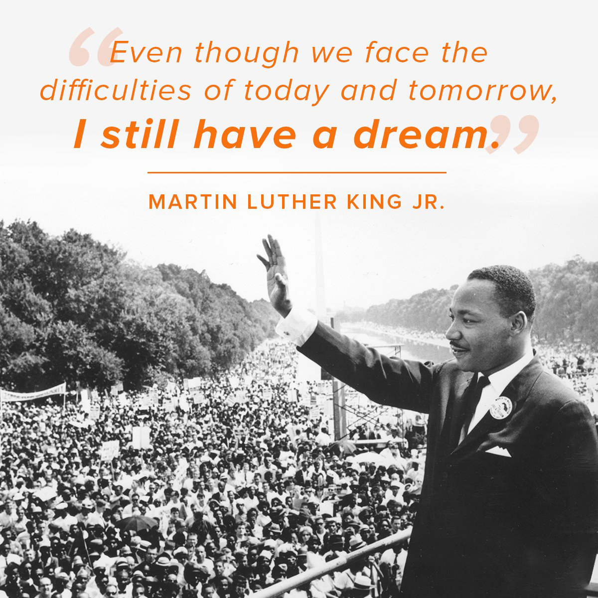 Black-and-white photo of Martin Luther King Jr. standing at a podium and waving to a large crowd gathered along the National Mall. Above him is an orange quote that reads, βEven though we face the difficulties of today and tomorrow, I still have a dream.β The quote is attributed to Martin Luther King Jr