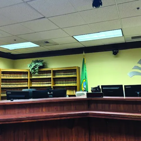 Judge's seat in the courtroom, computers behind and elevated desk with a bookshelf in the background